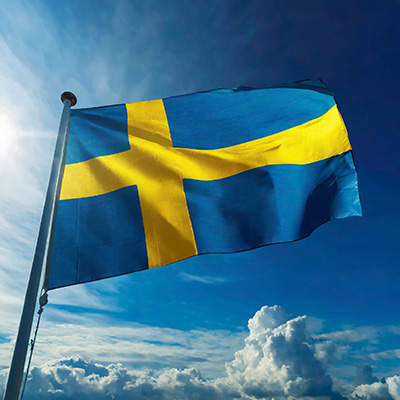 Swedish flag flying against a blue sky speckled with clouds.